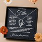 Necklace with heart design on a black plaque with French text, surrounded by flowers.
