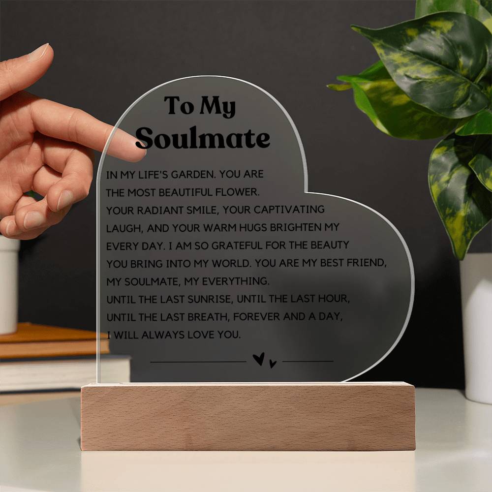 The image depicts a decorative piece consisting of a heart-shaped clear acrylic panel with text on it, mounted on a wooden base. The heart-shaped panel features a message addressed "To My Soulmate