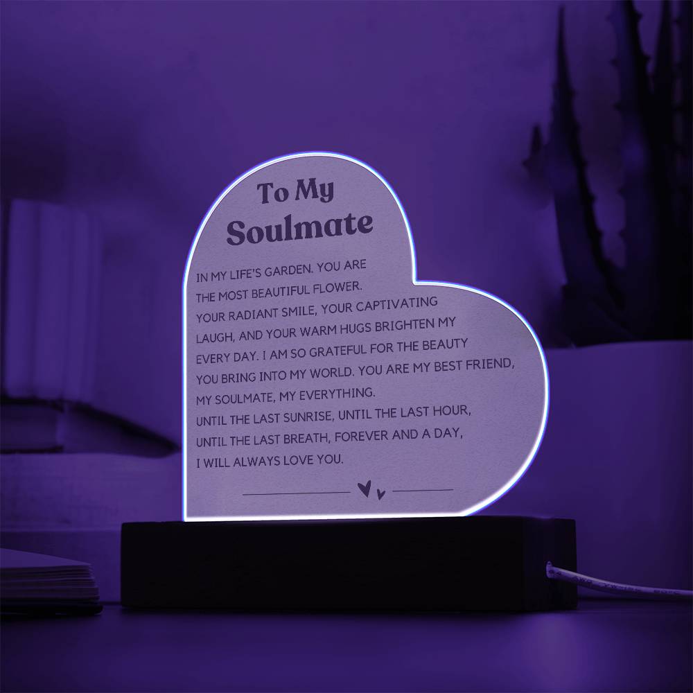 The image depicts a decorative piece consisting of a heart-shaped clear acrylic panel with text on it, mounted on a wooden base. The heart-shaped panel features a message addressed "To My Soulmate