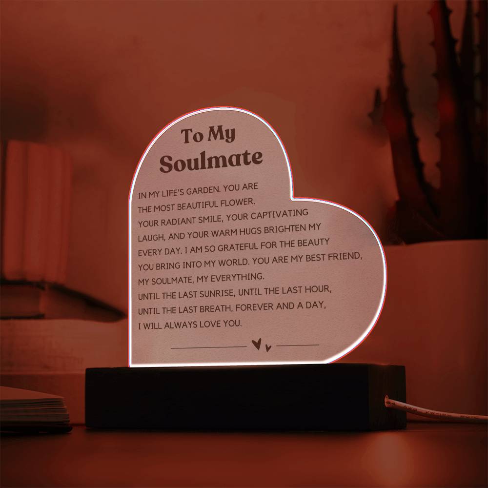 The image depicts a decorative piece consisting of a heart-shaped clear acrylic panel with text on it, mounted on a wooden base. The heart-shaped panel features a message addressed "To My Soulmate