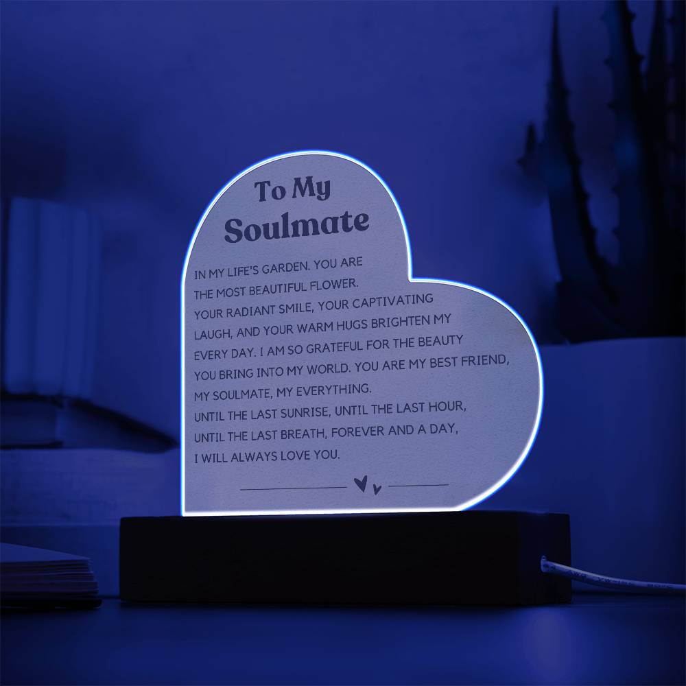 The image depicts a decorative piece consisting of a heart-shaped clear acrylic panel with text on it, mounted on a wooden base. The heart-shaped panel features a message addressed "To My Soulmate