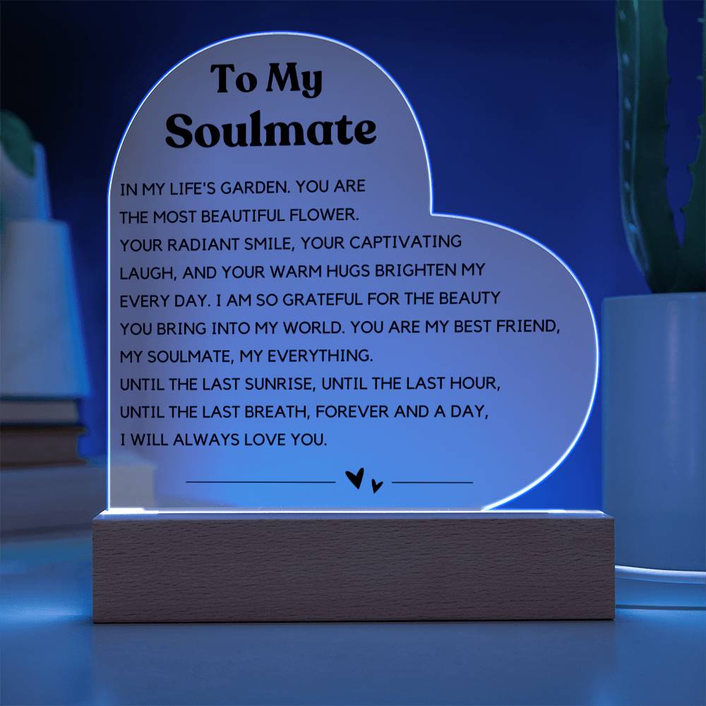 The image depicts a decorative piece consisting of a heart-shaped clear acrylic panel with text on it, mounted on a wooden base. The heart-shaped panel features a message addressed "To My Soulmate