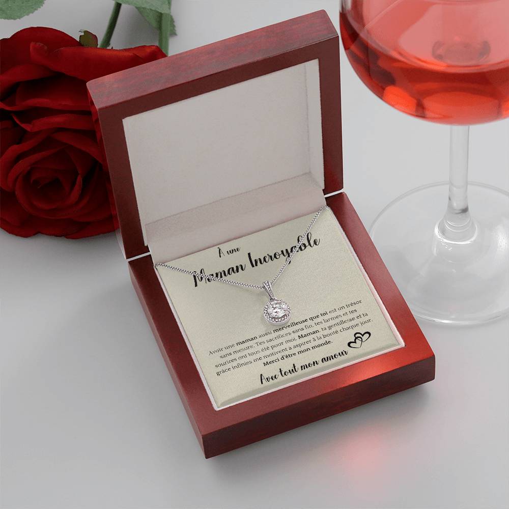 The image shows a card with a silver necklace featuring a round pendant with a central gemstone. The card reads "À une Maman Incroyable" at the top, with a heartfelt French message about the mother's sacrifices and kindness. It ends with "Avec tout mon amour" and a heart illustration.