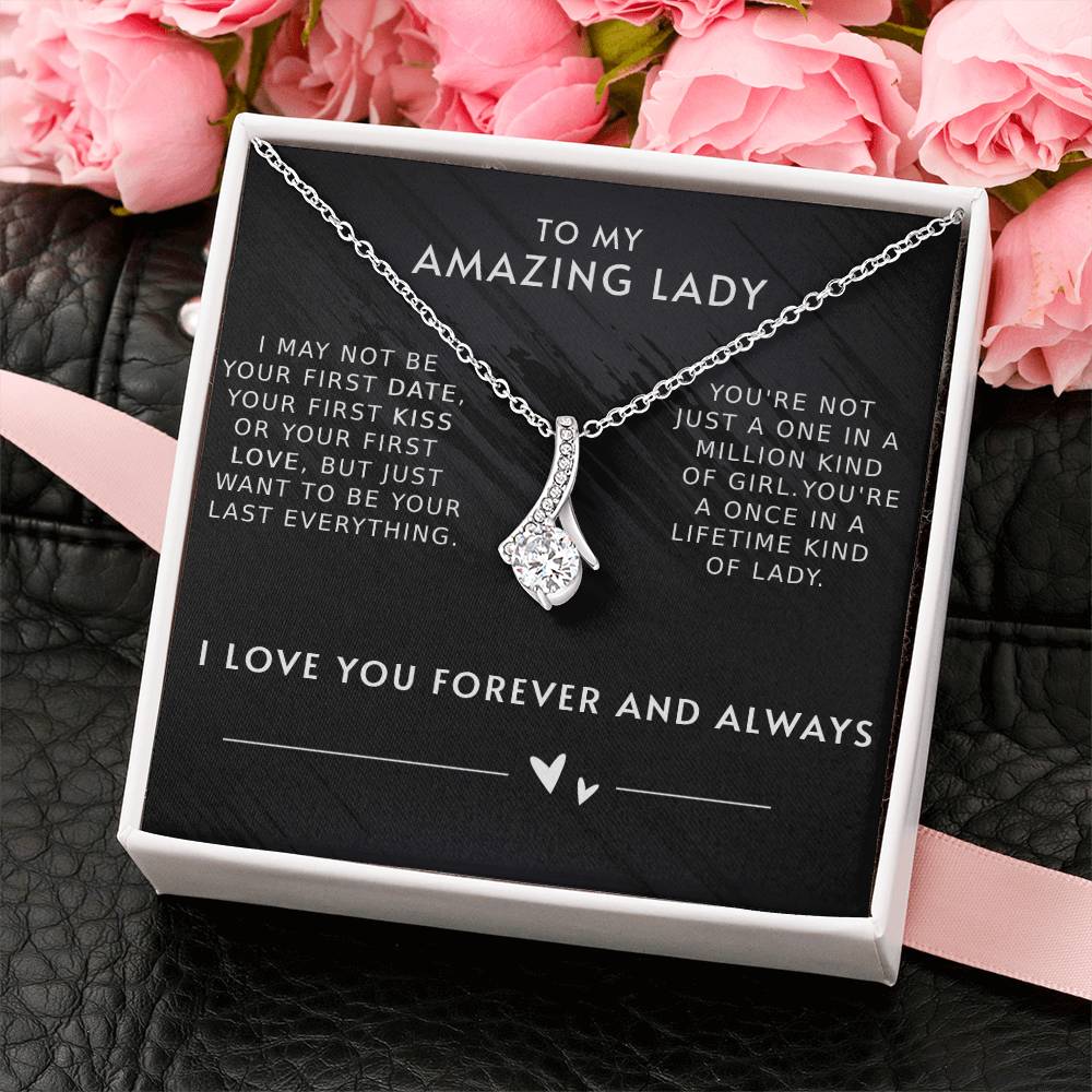 A necklace with a gemstone pendant in an open jewelry box with a loving message printed inside for girlfriend