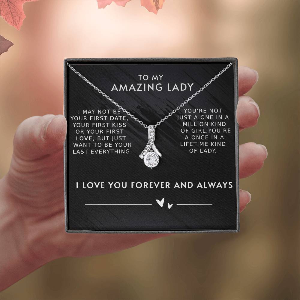 A necklace with a gemstone pendant in an open jewelry box with a loving message printed inside for girlfriend