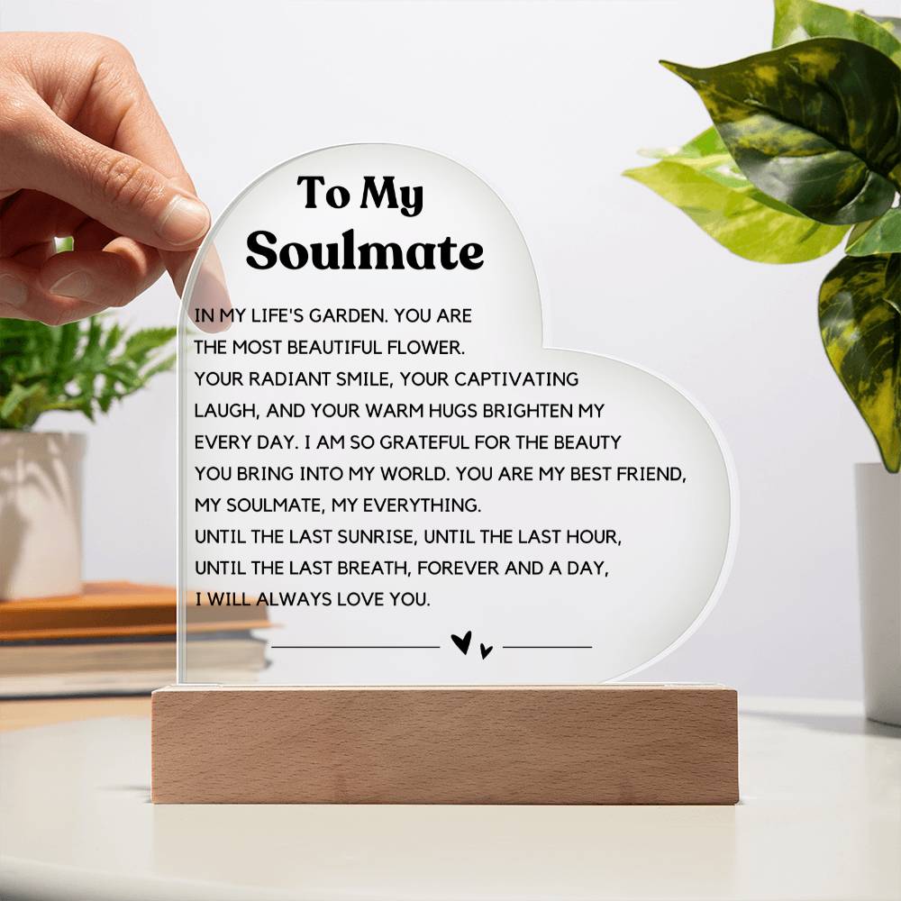 The image depicts a decorative piece consisting of a heart-shaped clear acrylic panel with text on it, mounted on a wooden base. The heart-shaped panel features a message addressed "To My Soulmate