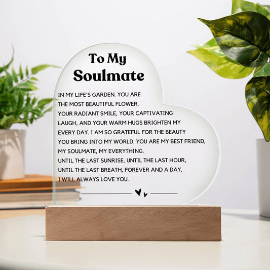 The image depicts a decorative piece consisting of a heart-shaped clear acrylic panel with text on it, mounted on a wooden base. The heart-shaped panel features a message addressed "To My Soulmate