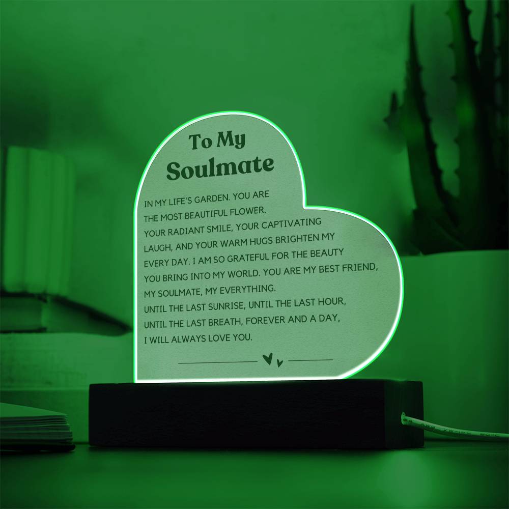 The image depicts a decorative piece consisting of a heart-shaped clear acrylic panel with text on it, mounted on a wooden base. The heart-shaped panel features a message addressed "To My Soulmate